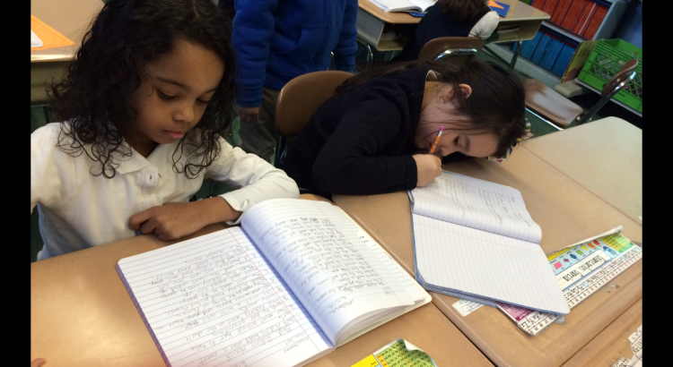 Two girls are writing in a book at the table.